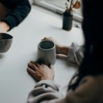 Due persone al tavolo tengono in mano tazze durante una conversazione; immagine illustrativa dell'ascolto senza fretta. Foto: Priscilla Du Preez / Unsplash.