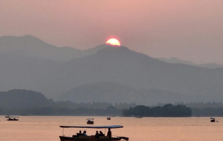 Una barca scivola sul lago nella luce del tramonto: immagine evocativa del paesaggio cinese; foto illustrativa di Frudrax Cheng su Unsplash.