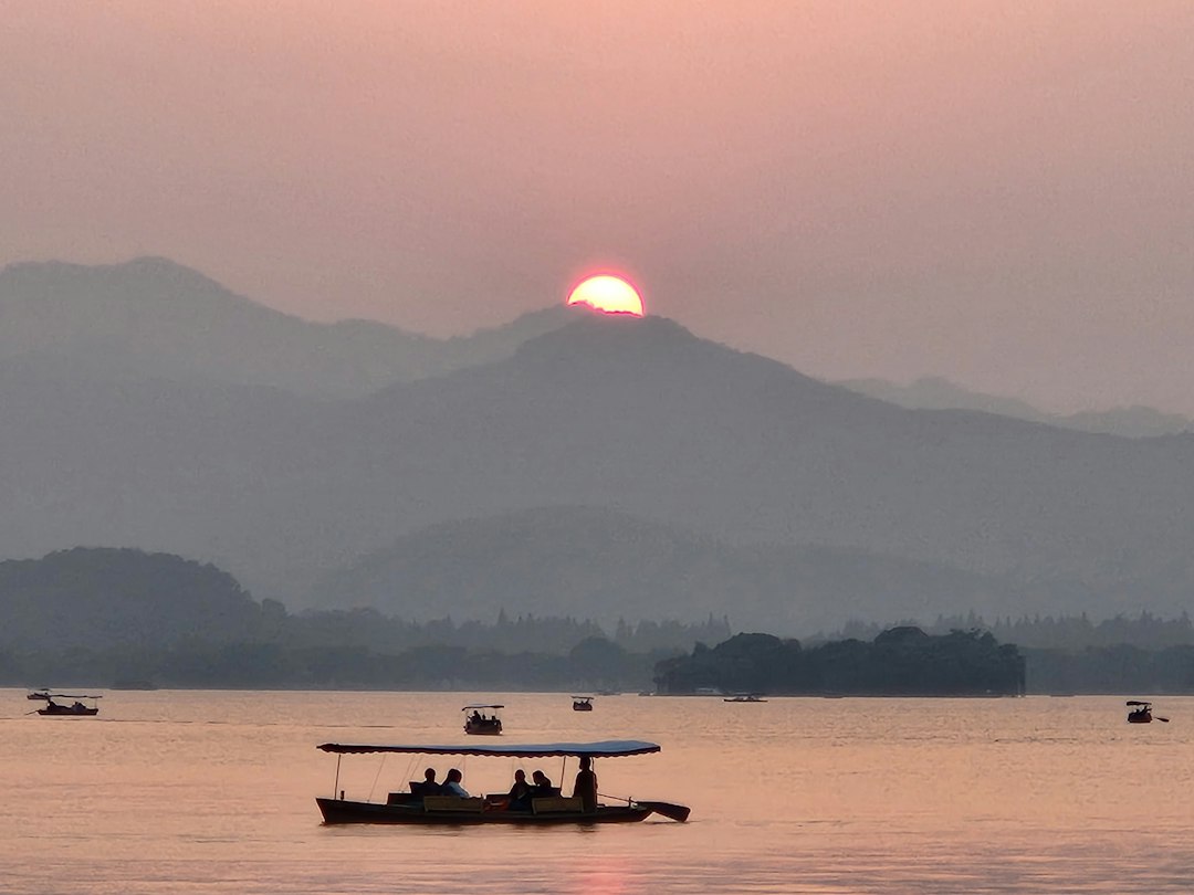 Una barca scivola sul lago nella luce del tramonto: immagine evocativa del paesaggio cinese; foto illustrativa di Frudrax Cheng su Unsplash.