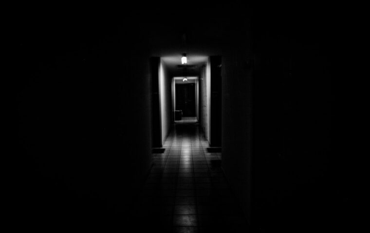 Corridoio in ombra con luce in fondo, immagine simbolica della possibilità di uscire dallo sfruttamento. Foto MARIOLA GROBELSKA, Unsplash.