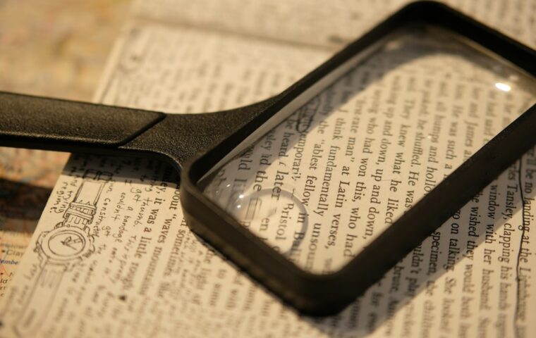 Lente d'ingrandimento appoggiata su testo stampato: immagine illustrativa della verifica delle informazioni, foto di Spencer Liao su Unsplash